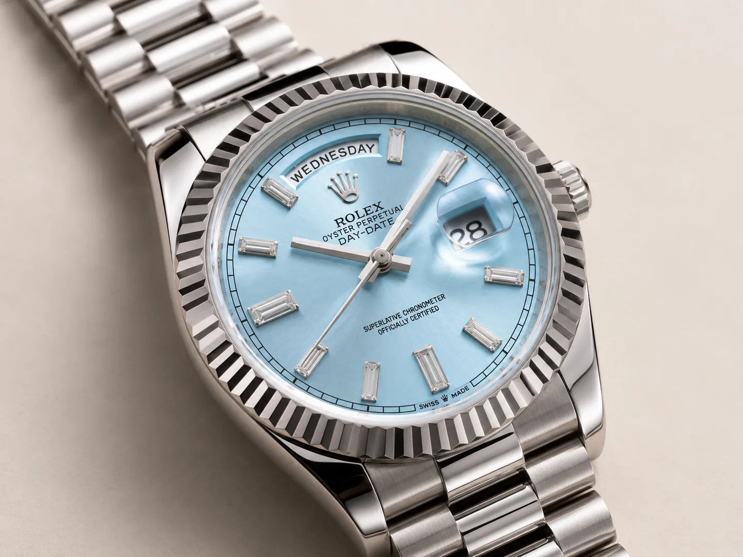 Close-up of a Rolex Day-Date watch featuring an ice blue sunburst dial, fluted bezel, baguette-cut hour markers, day display at 12 o’clock, and magnified date window, captured in a luxury studio setting.