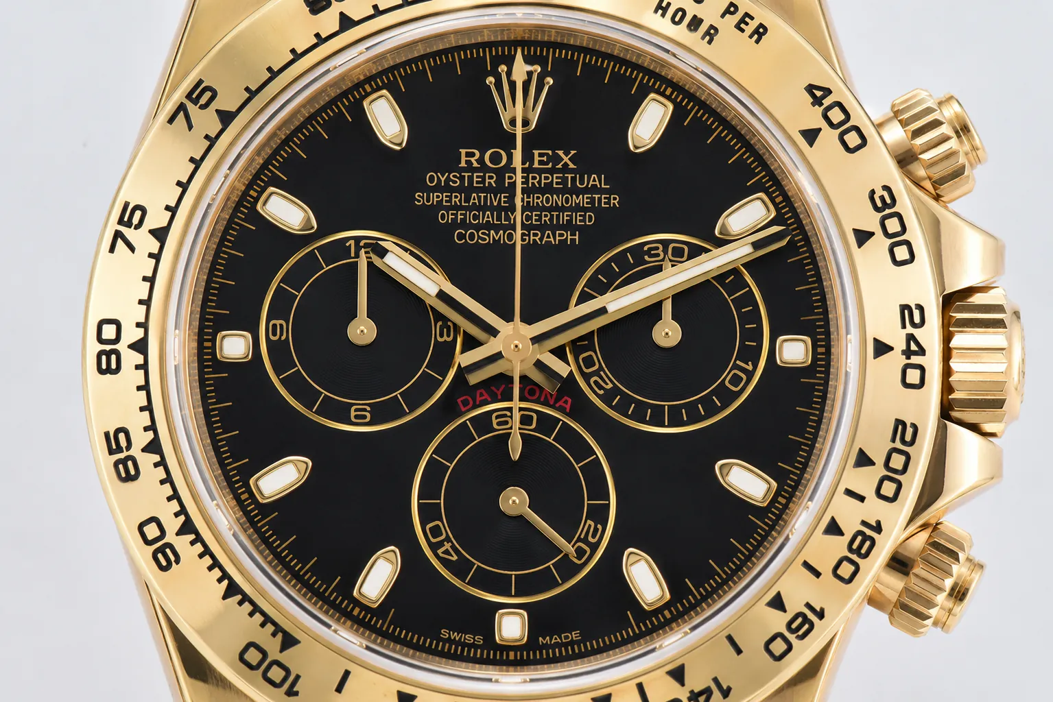 Macro close-up of a gold Rolex Daytona chronograph dial featuring a black face, gold-tone subdials, engraved tachymeter bezel, luminous hour markers, and premium yellow gold craftsmanship.