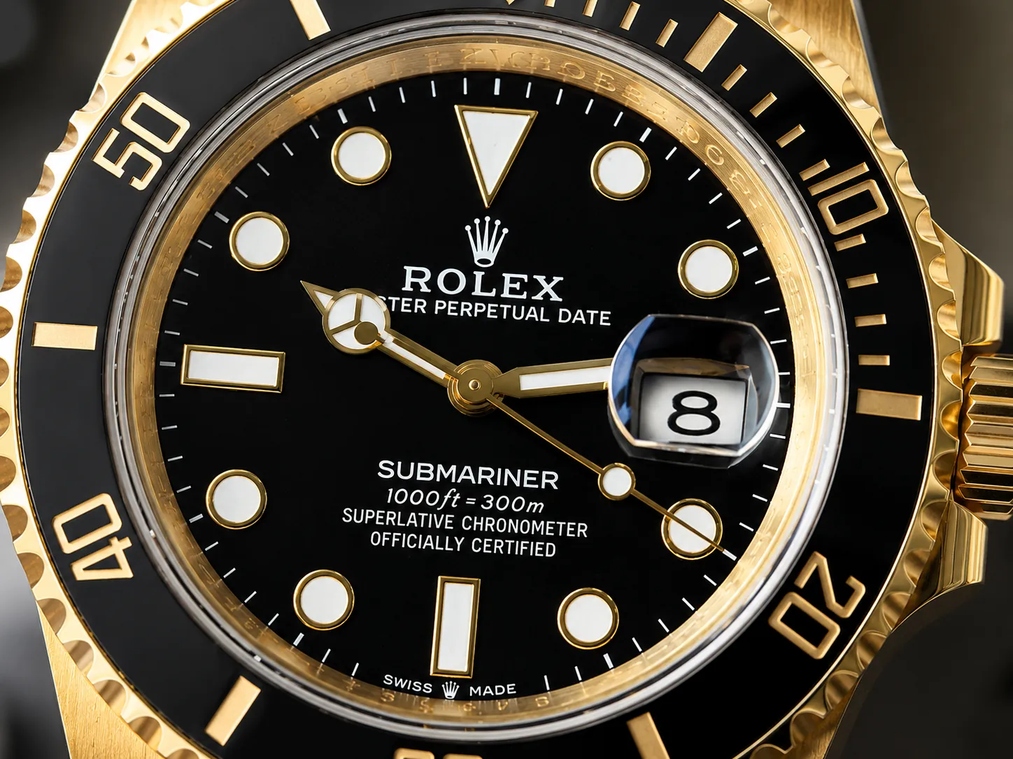 Macro close-up of a gold Rolex Submariner watch dial featuring a black face, luminous hour markers, Mercedes hands, magnified date window, and black ceramic dive bezel with gold accents.