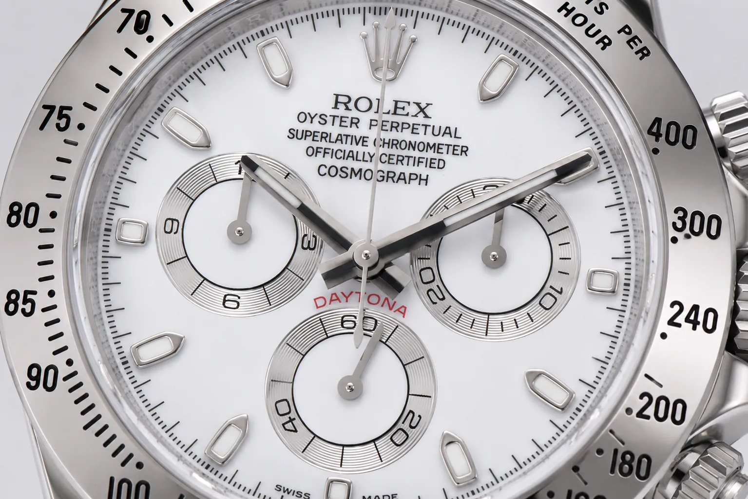 Macro close-up of a Rolex Daytona chronograph dial featuring a white face, three recessed subdials, polished hour markers, tachymeter bezel, and stainless steel case craftsmanship.