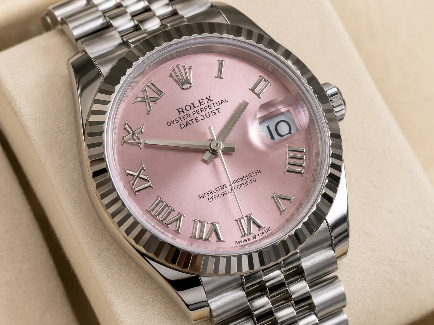 Close-up of a Rolex Datejust watch featuring a pink sunburst dial, Roman numeral hour markers, fluted bezel, Jubilee bracelet, and magnified date window, displayed in a luxury studio setting.